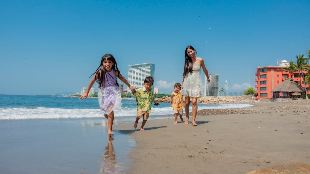 A joyful family playing on a sunny beach with waves and skyscrapers in the background.
