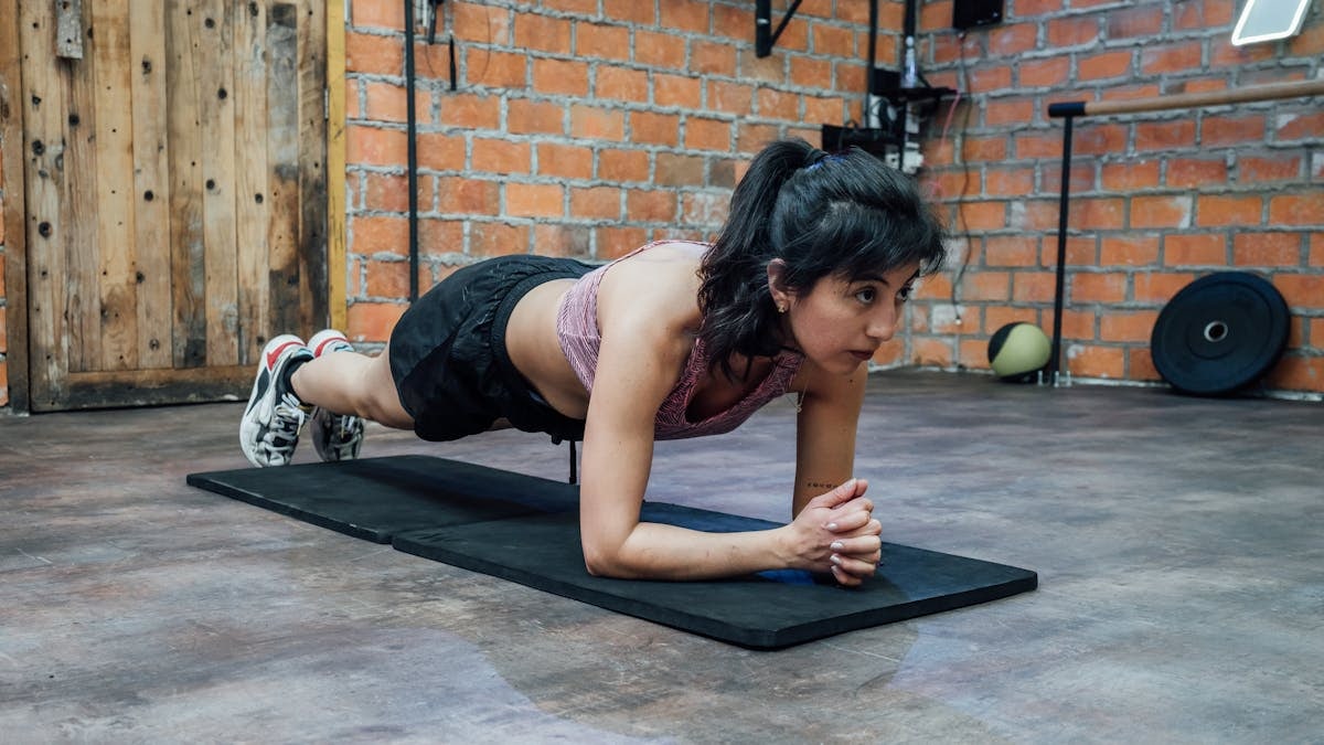 A woman doing a plank workout in a brick-walled gym, showcasing fitness and strength in Mexico City.
